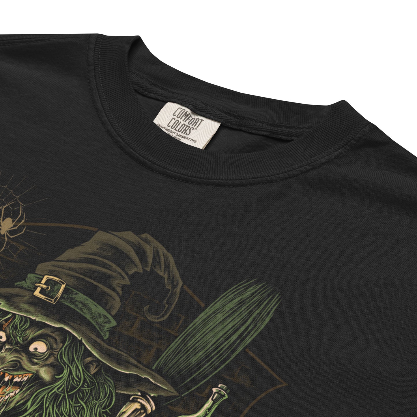 A close up of a black t-shirt with a graphic print of a witch and a pumpkin cauldron surrounded by spooky elements like skulls and a black cat.