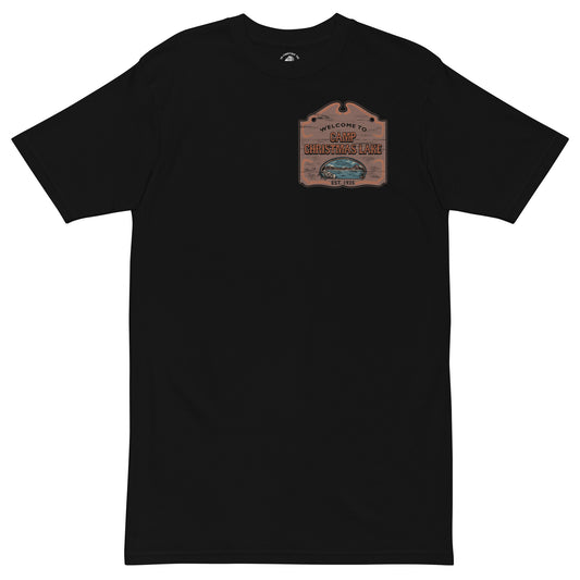 Product mockup featuring a black t-shirt with a wooden sign on the chest that says "Welcome to Camp Christmas Lake"