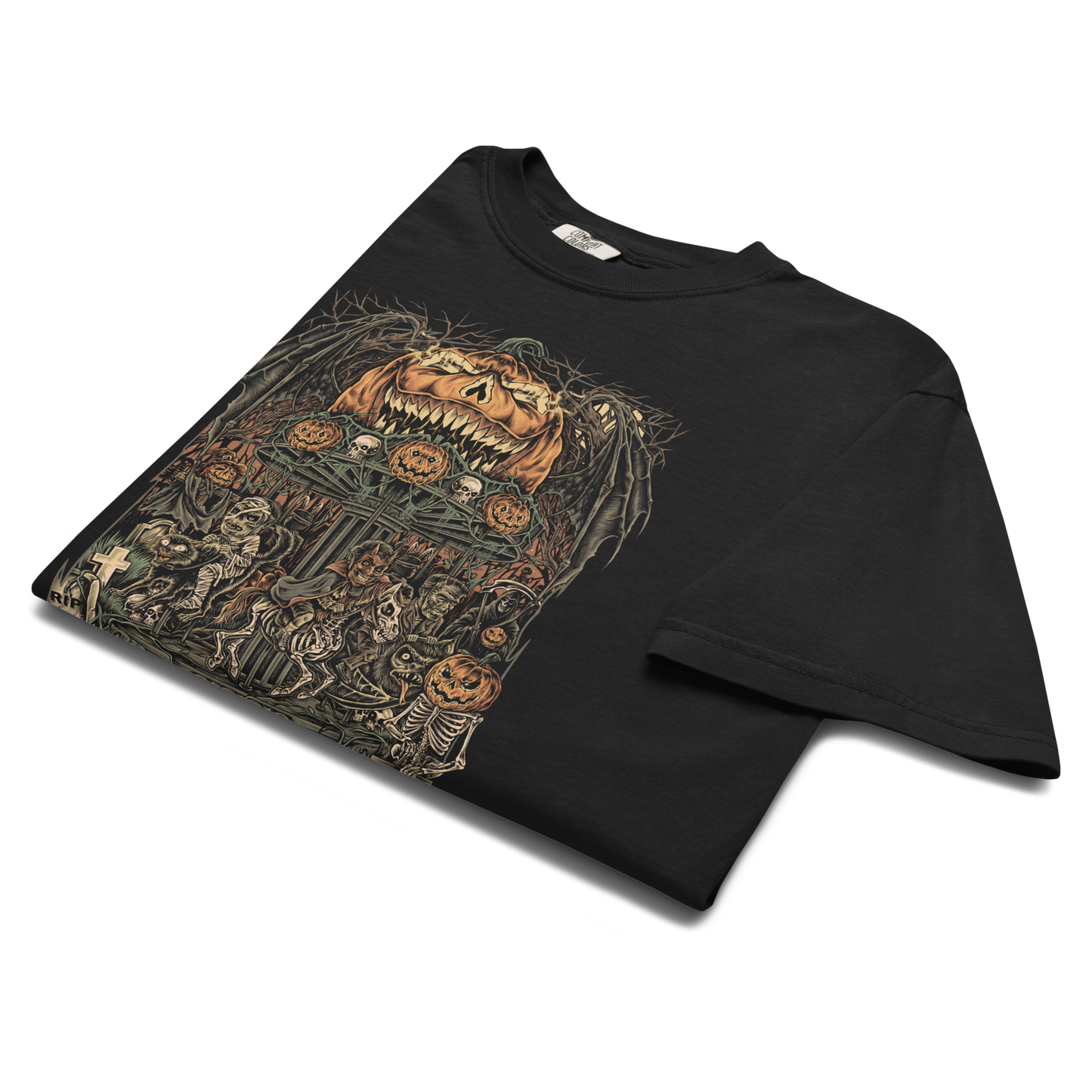 Black folded halloween T‑shirt featuring a haunted carnival carousel made of jack‑o’‑lanterns with skeletal horses, skulls, bats, and a gravestone under a giant grinning pumpkin head.